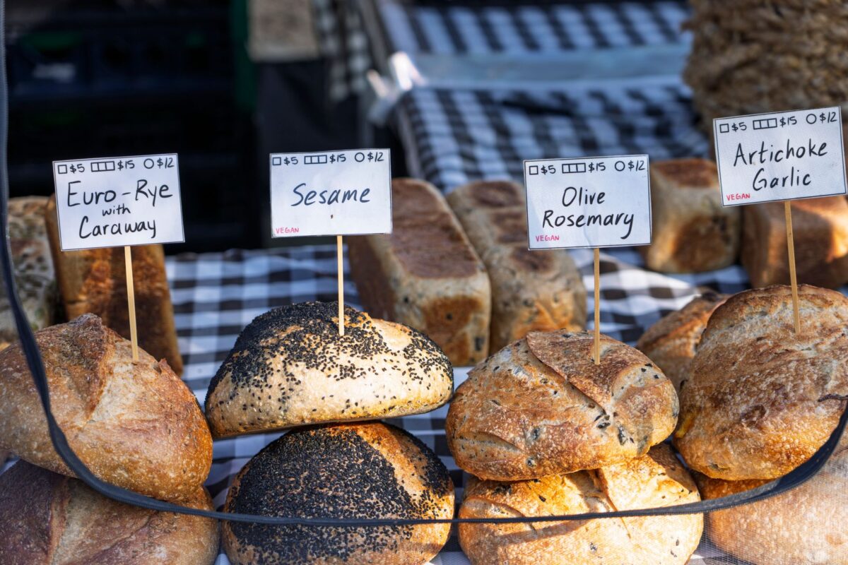 Assorted artisanal breads on display at a market stall, labeled with prices and ingredients, related to kalonji price in pakistan