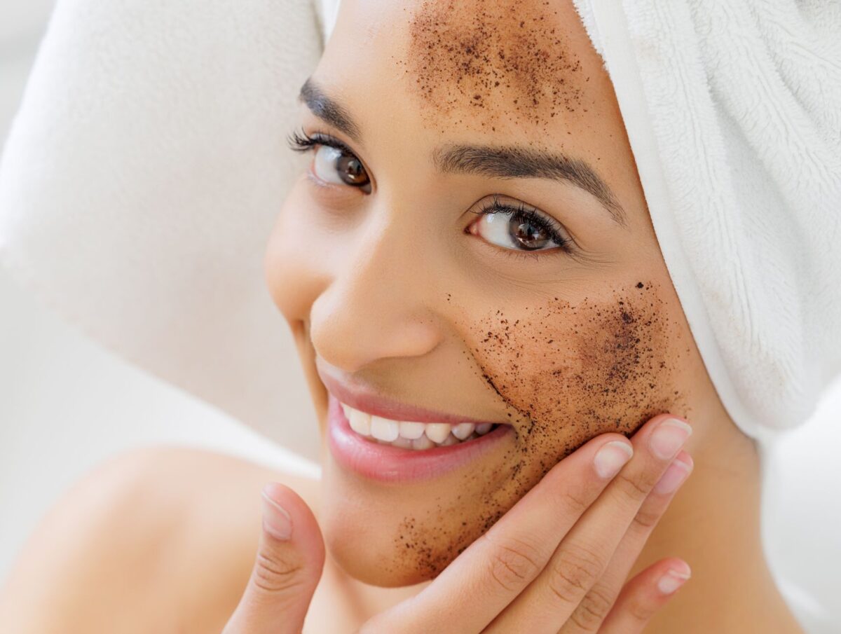 Smiling woman with towel on her head applying a natural exfoliating face mask. Skincare and self-care concept, related to Shilajit honey syrup for skin benefits