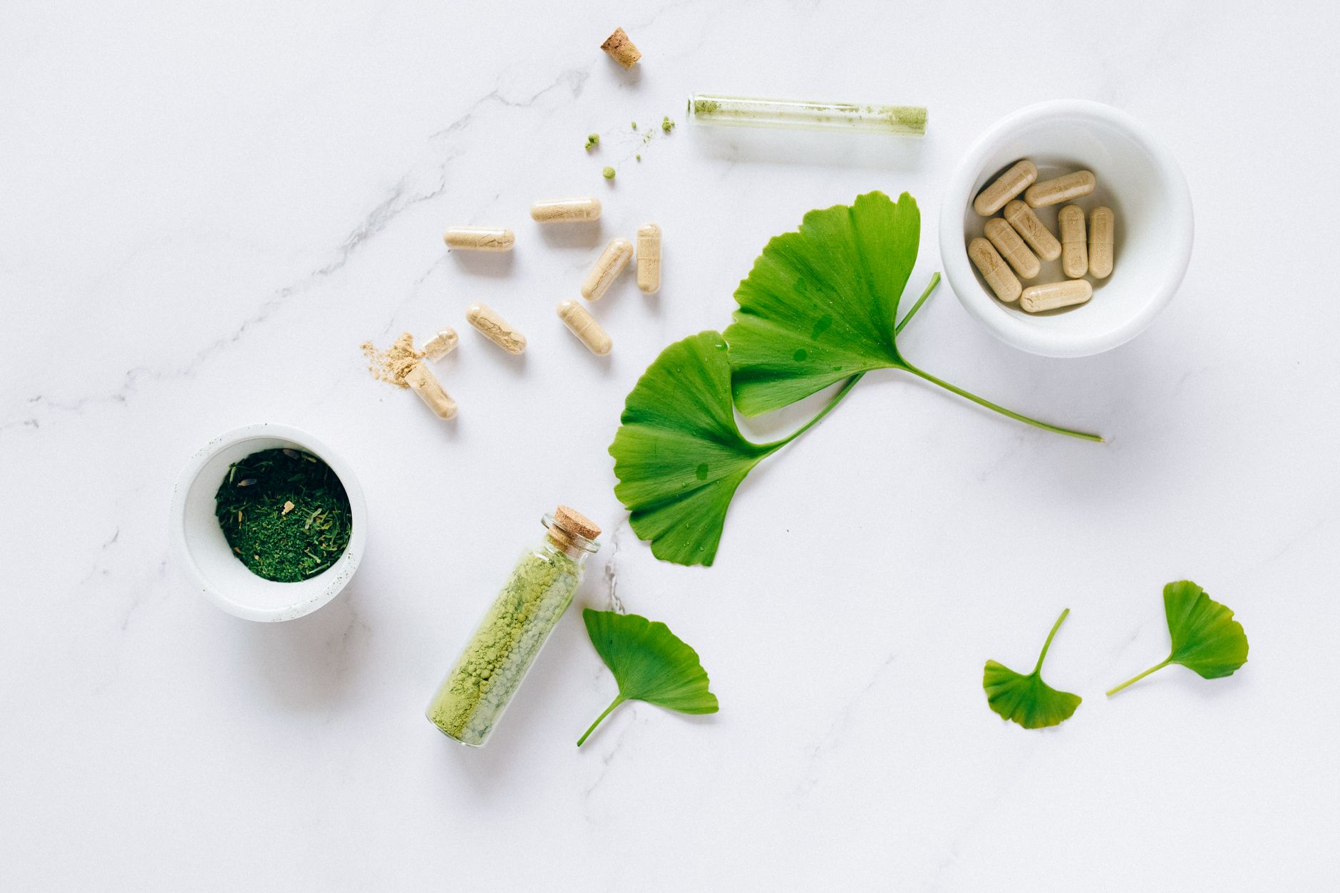 Shilajit honey syrup heart health benefits – Flat lay of herbal supplements with ginkgo leaves on marble surface, emphasizing natural health remedies.