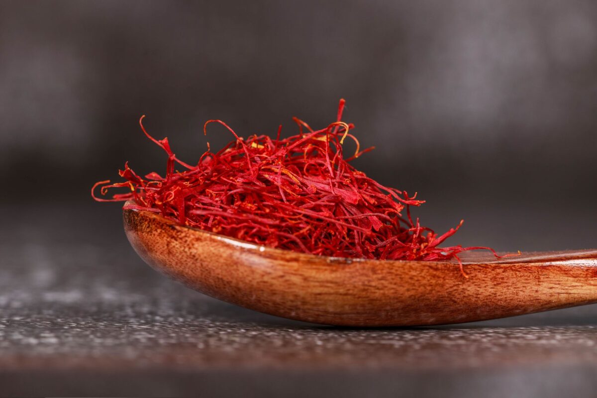 Detailed close-up of vibrant saffron threads in a wooden spoon, perfect for culinary imagery, related to zafran original